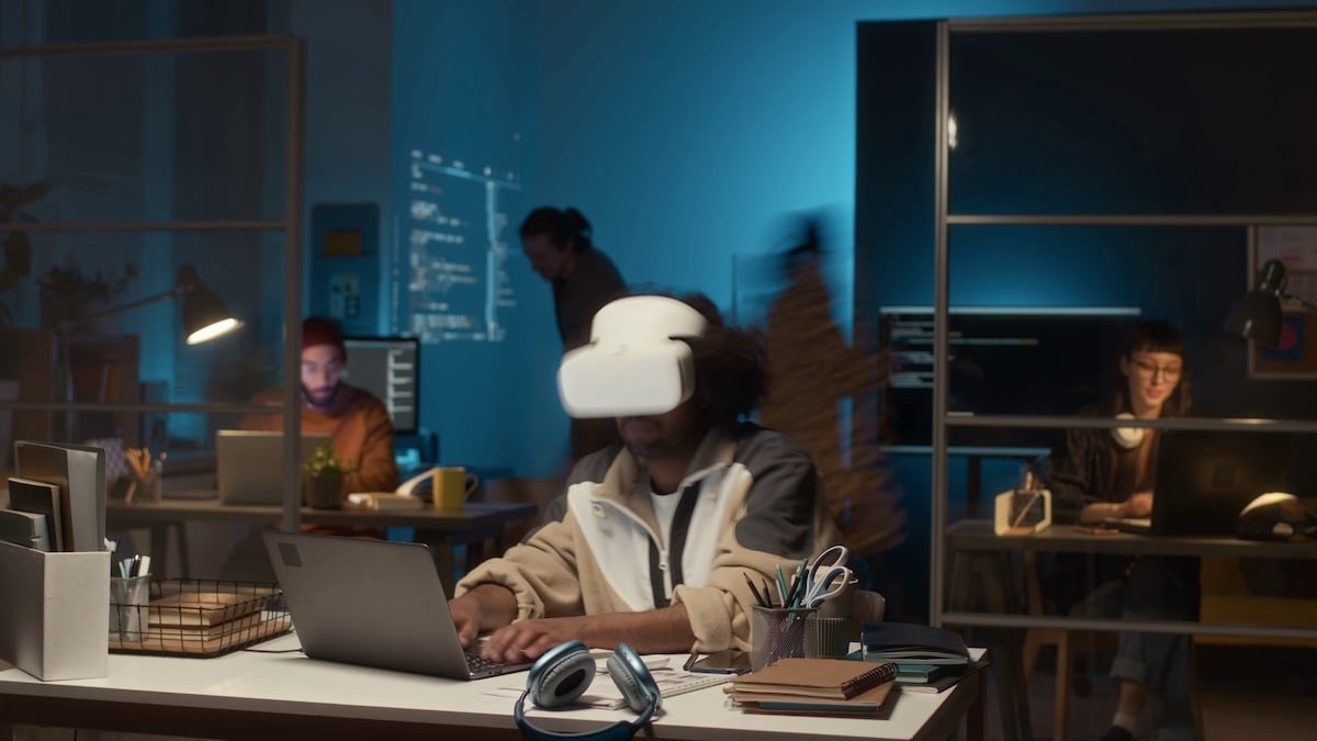 Timelapse shot of a young male programmer sitting at a desk at night, illuminated by multiple monitors and a dim room light, working intently on code